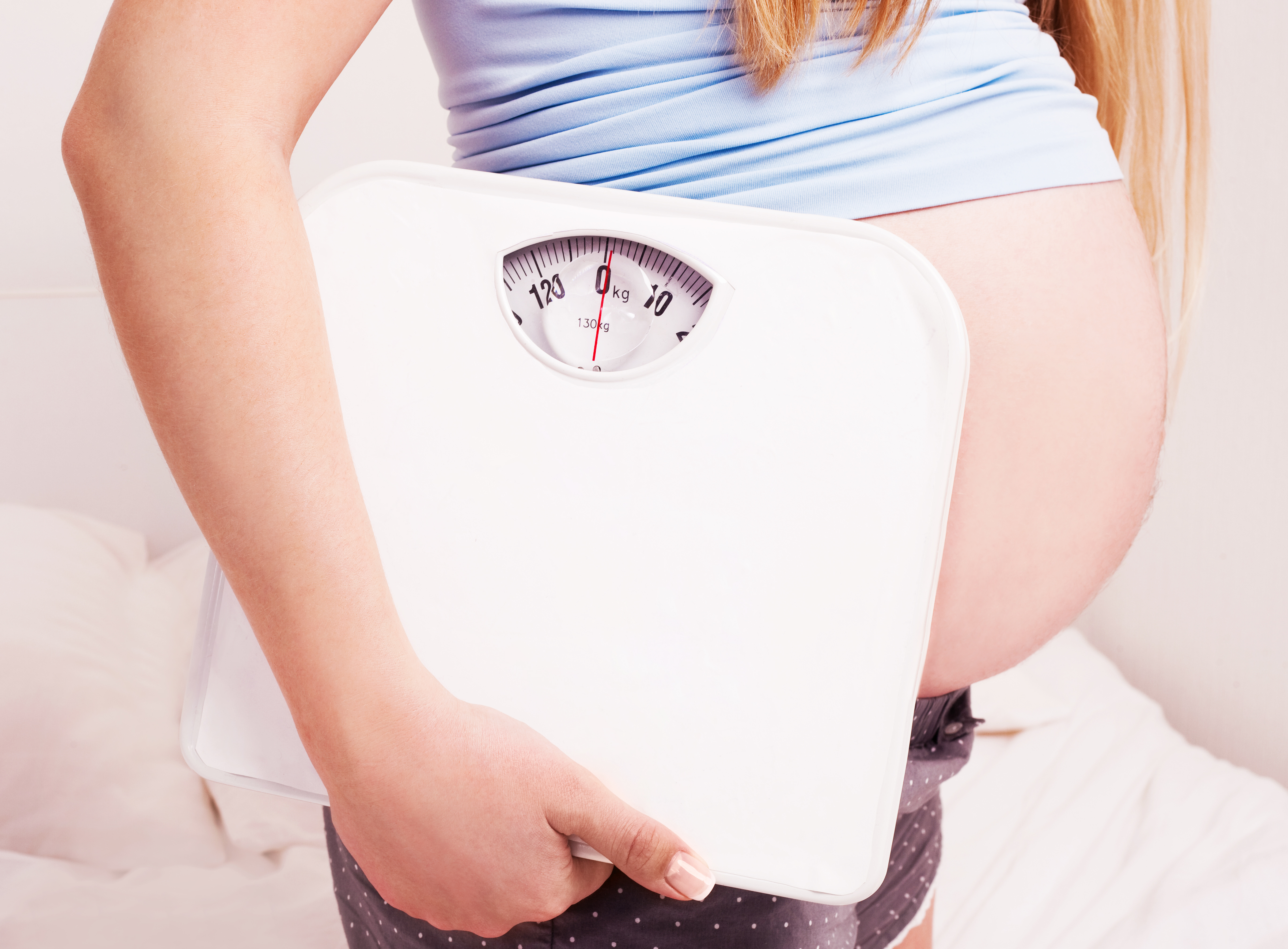 belly of a young pregnant woman holding scales  at home (focus on the scales)